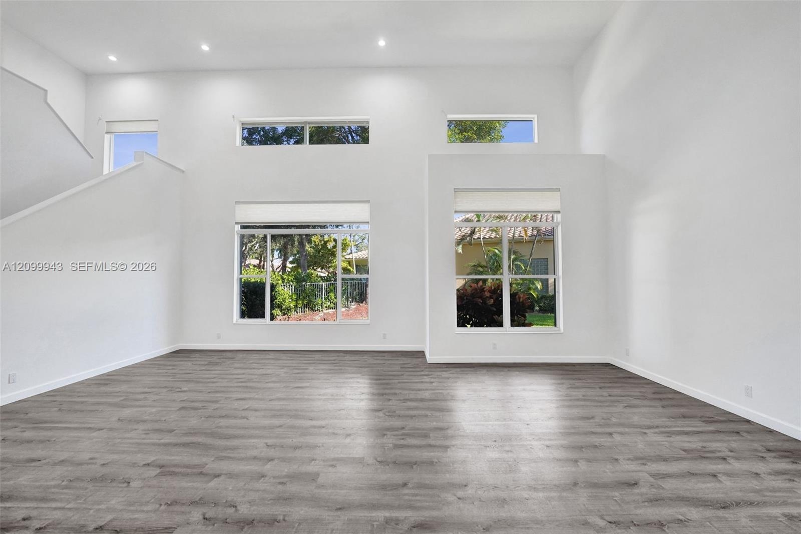 High-ceilinged interior space featuring wood-finish flooring, multi-level windows, and recessed lighting
