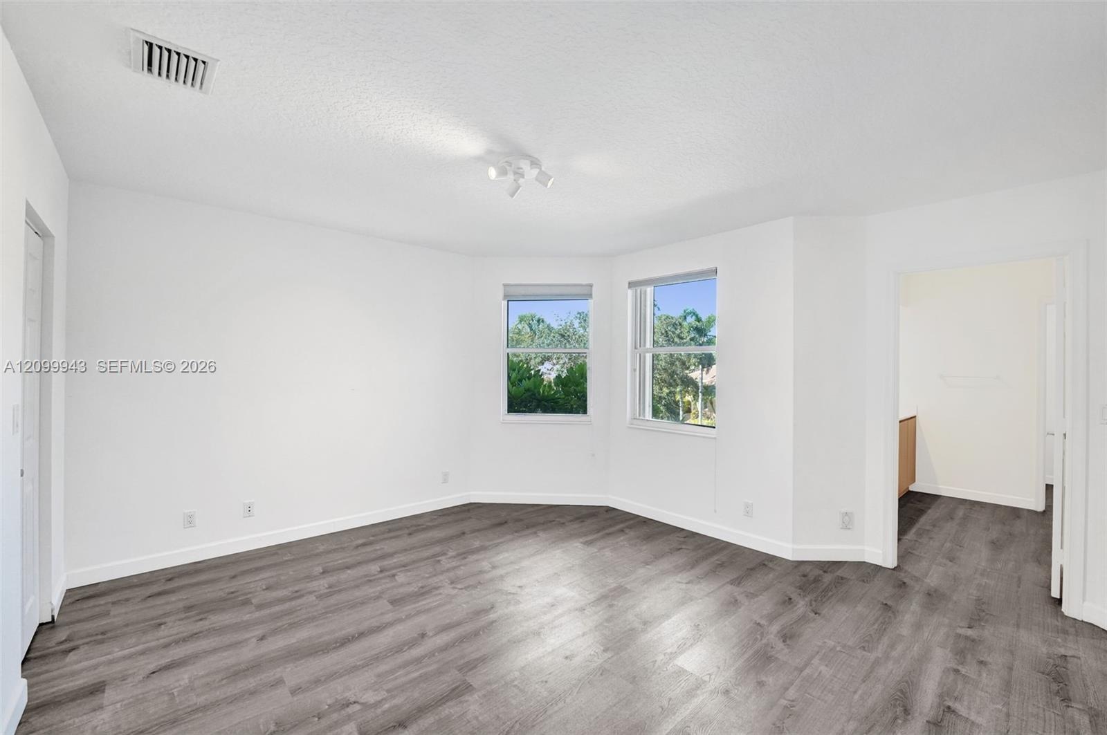 Room featuring wood-finish flooring, a multi-paneled bay window, and a ceiling-mounted light fixture