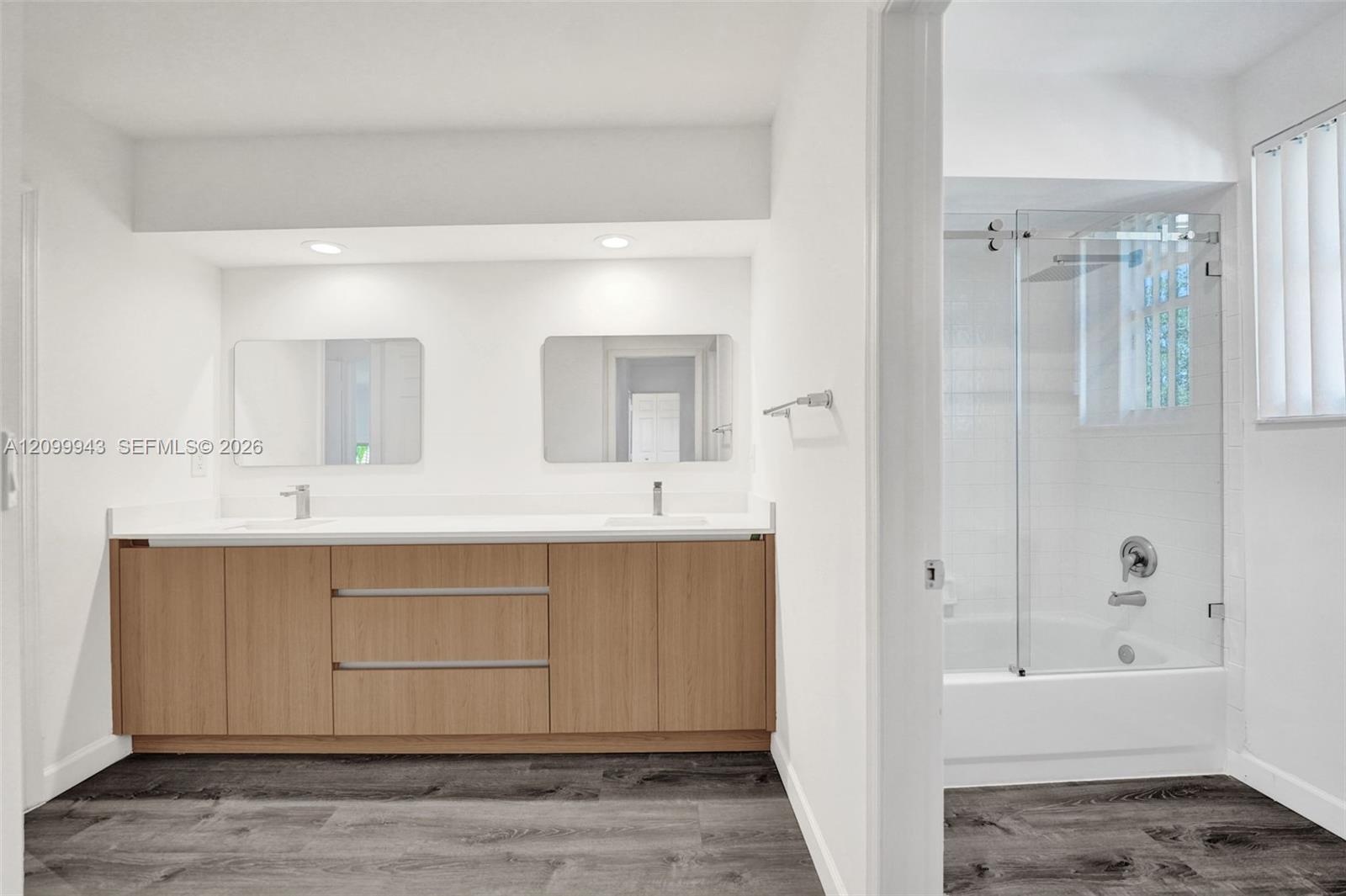 Double vanity featuring a wood-finish cabinet, dual rectangular undermount sinks, frameless mirrors, and a tub-shower combination with a sliding glass