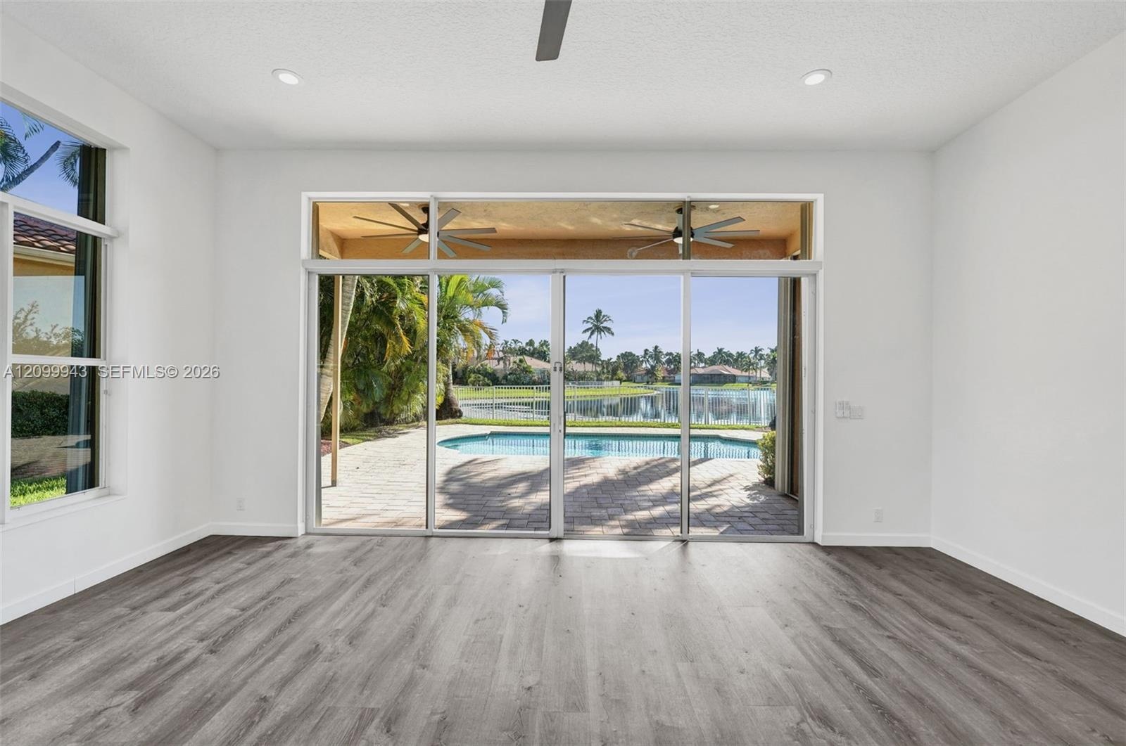 Wood-finish flooring, recessed lighting, ceiling fan, expansive sliding glass doors, and water-front swimming pool