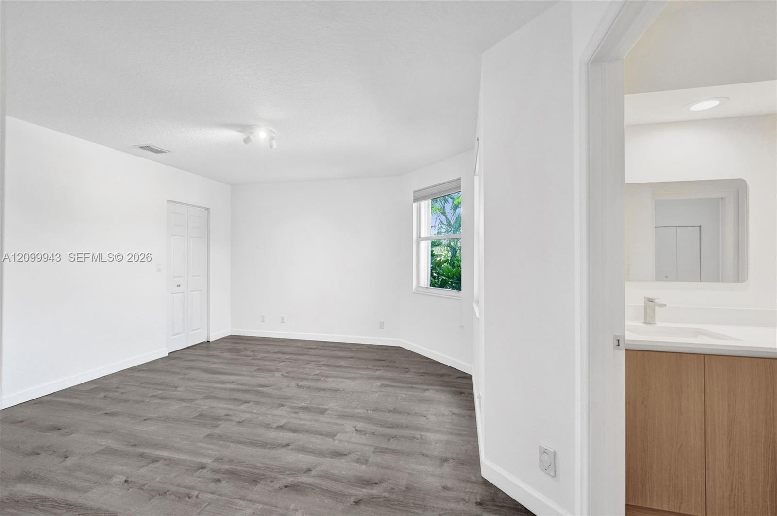 Neutral-toned interior featuring wood-finish flooring, a bay-style window, and a multi-panel closet door, with an attached bathroom showcasing a woode
