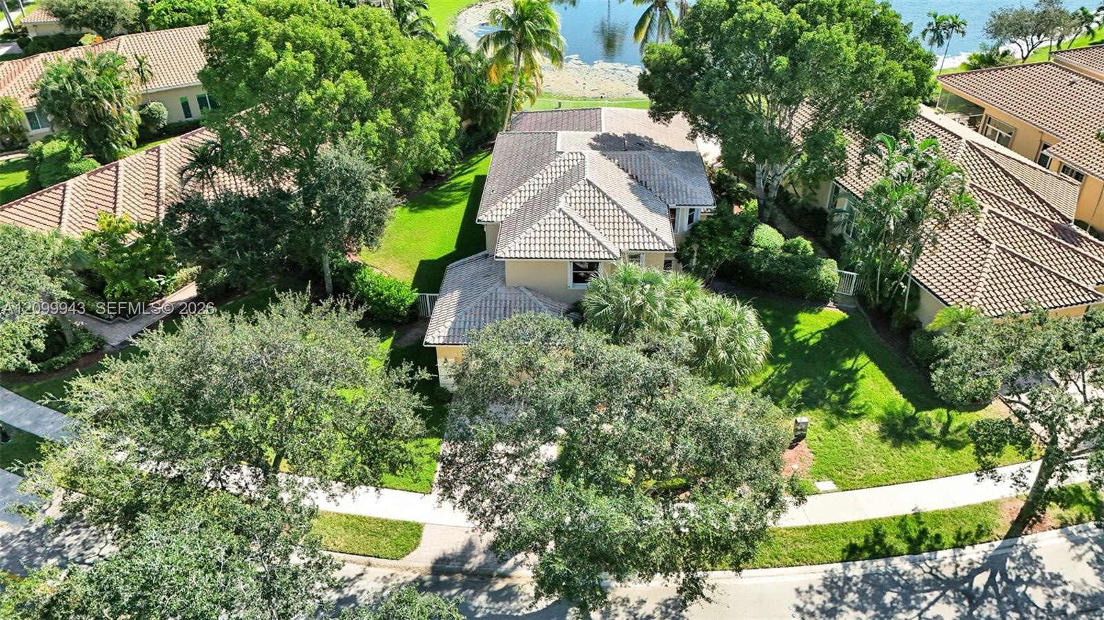 Aerial perspective of a multi-level residence featuring a multi-pitched tile roof, expansive grass lawn, mature shade trees, and waterfront positionin