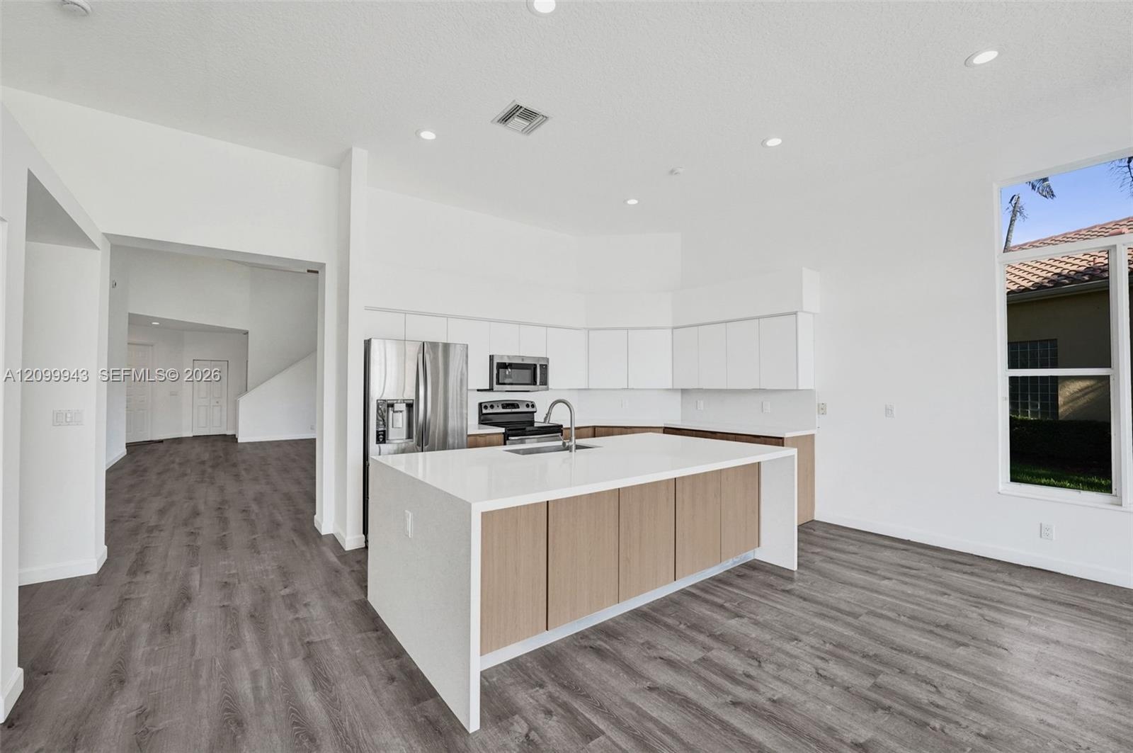 Kitchen featuring a large waterfall-edge center island, quartz countertops, dual-tone cabinetry, stainless steel appliances, and wood-finish flooring