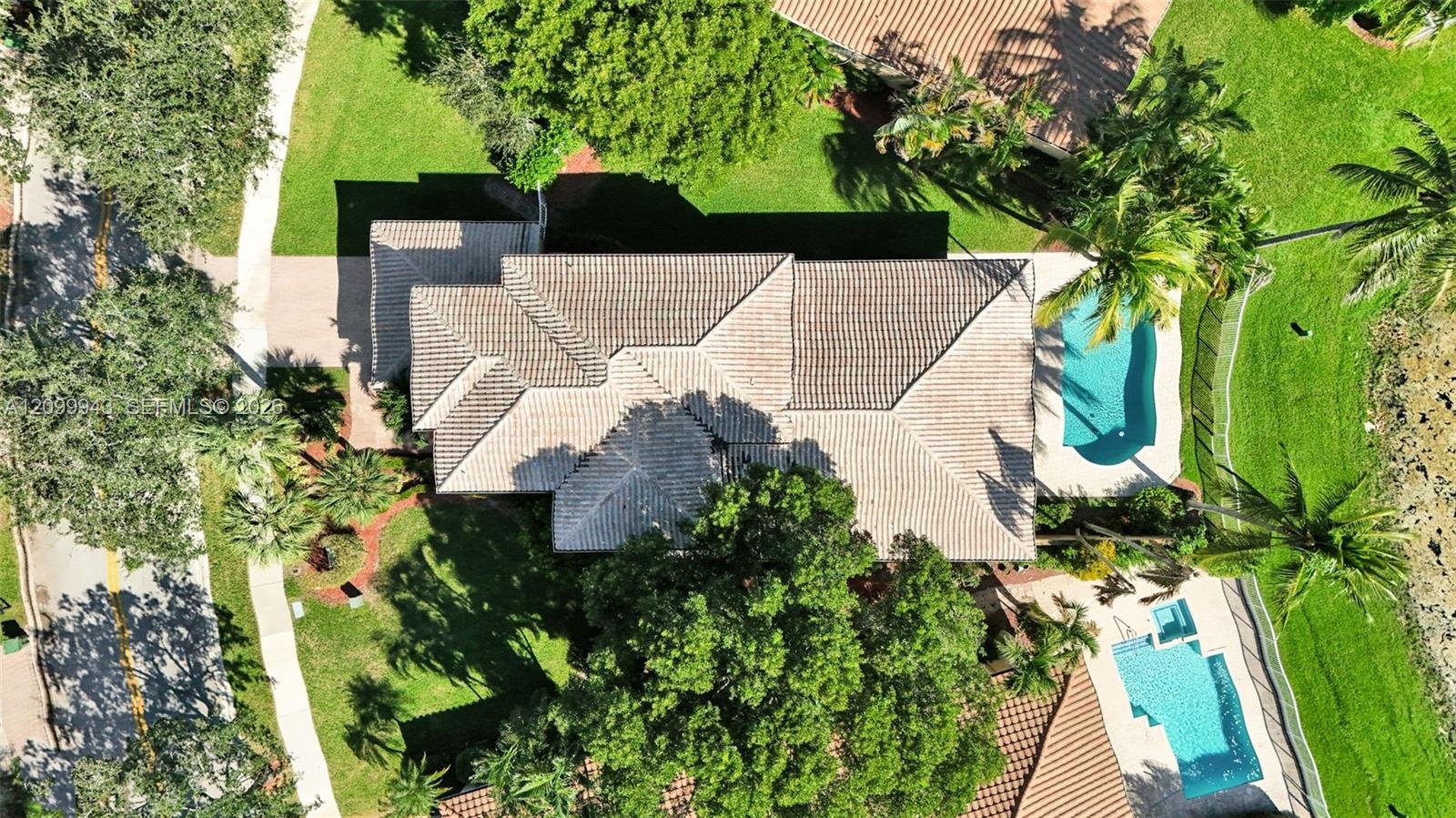Aerial perspective featuring a multi-hipped tile roof, an in-ground swimming pool, a separate in-ground spa, mature trees, and manicured landscaping