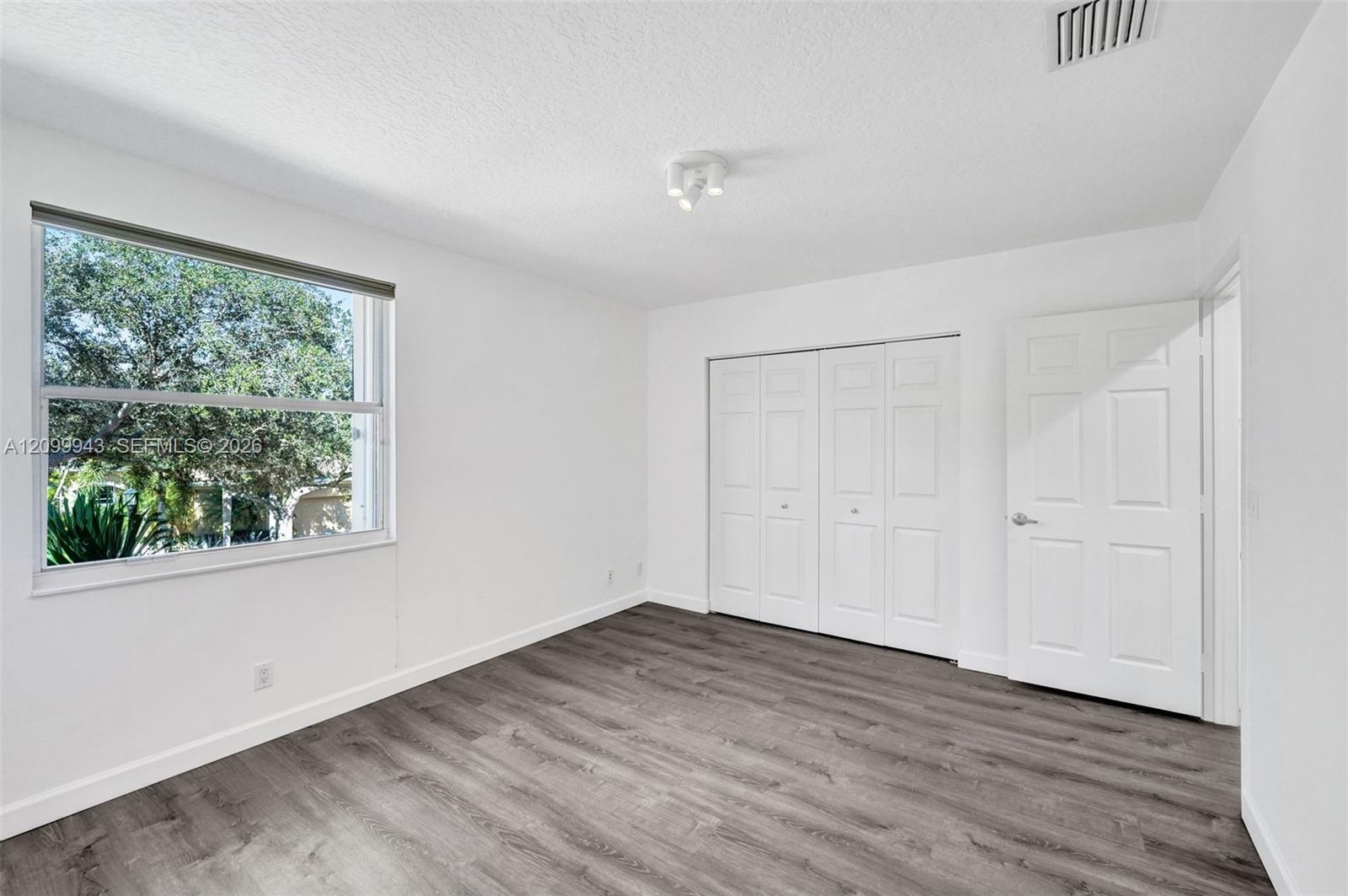 Room featuring wood-finish flooring, a multi-panel interior door, a floor-to-ceiling closet with bifold doors, and a single-pane window