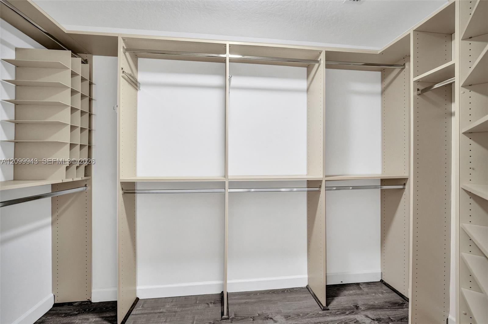 Walk-in closet featuring floor-to-ceiling built-in cabinetry, tiered shelving units, integrated hanging rods, and wood-finish flooring