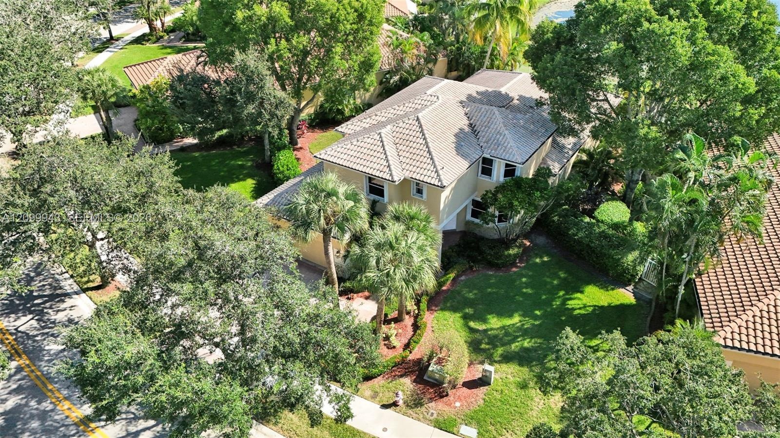 Two-story residence featuring a hipped tile roof, stucco exterior, paved driveway, mature landscaping, and a manicured lawn