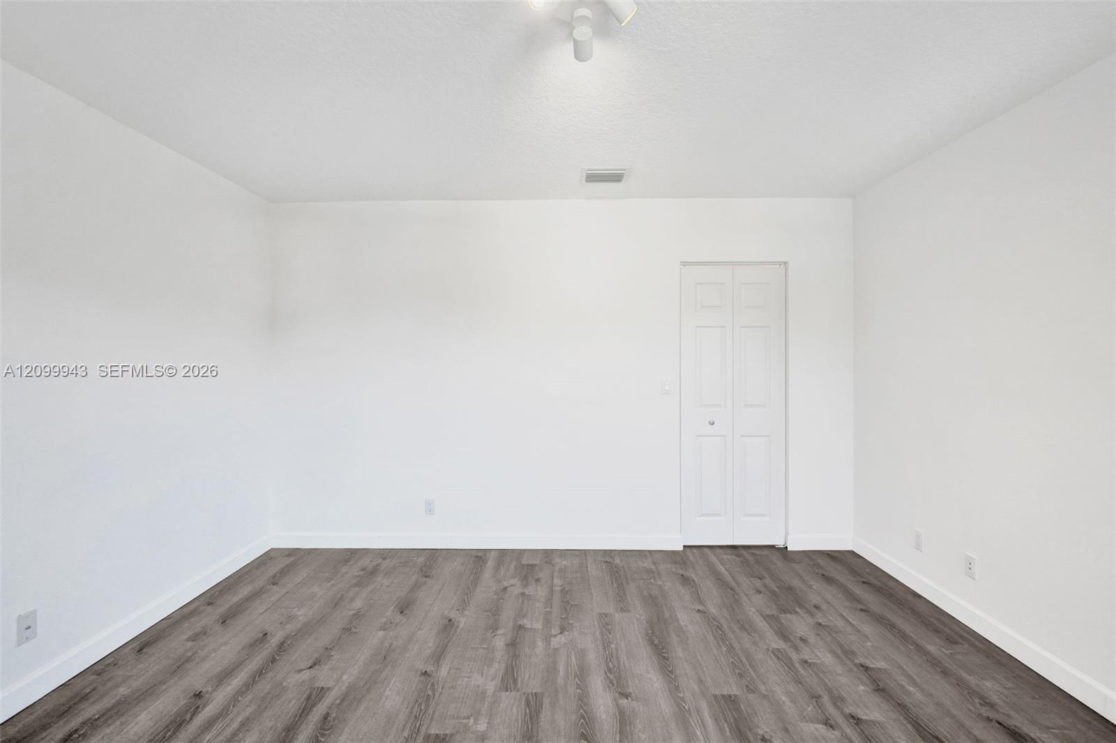 Neutral-toned interior space featuring wood-finish flooring, white walls, and a multi-panel bi-fold closet door