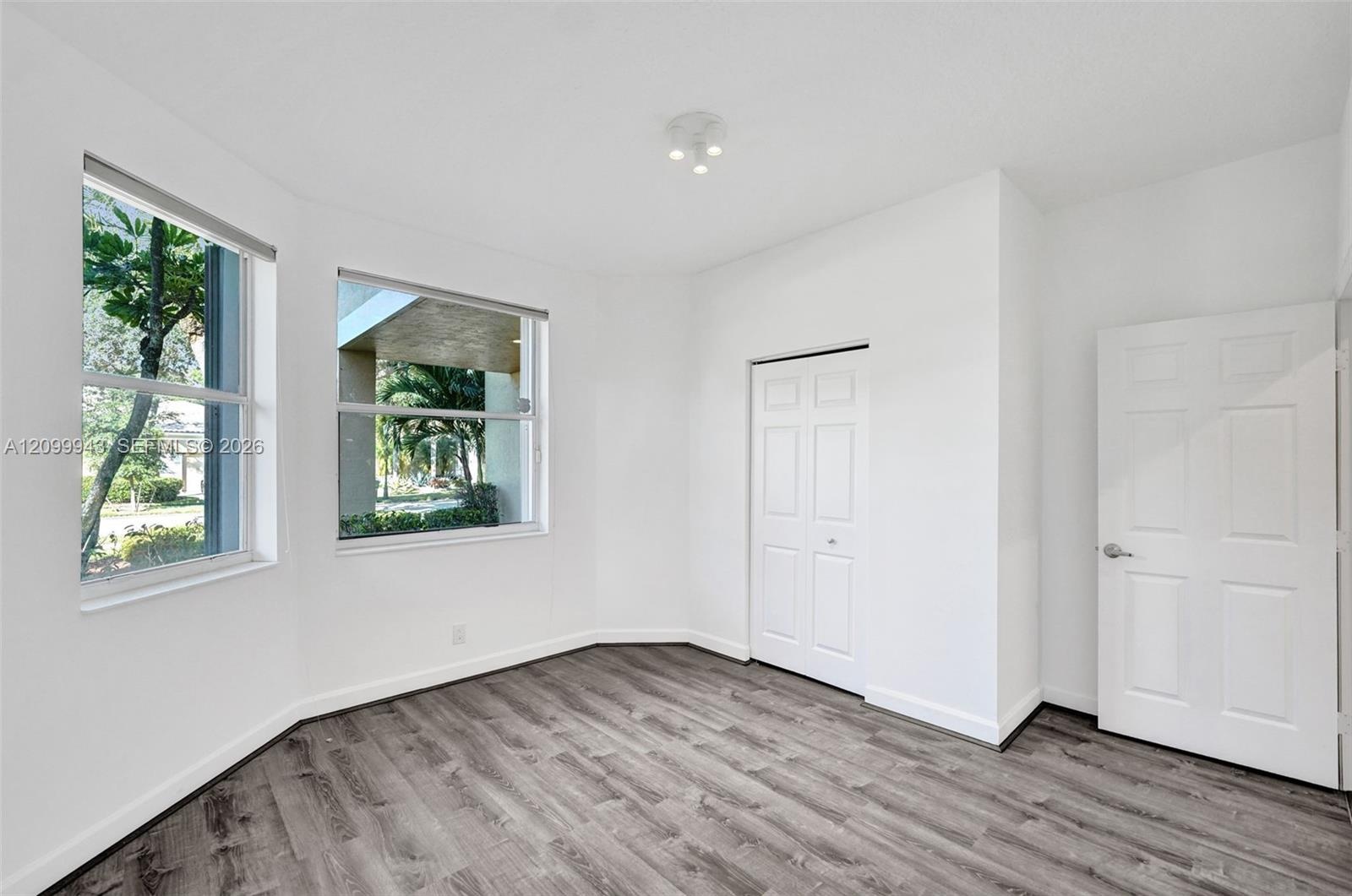 Room featuring wood-finish flooring, dual windows, ceiling-mounted light fixture, and two panel doors