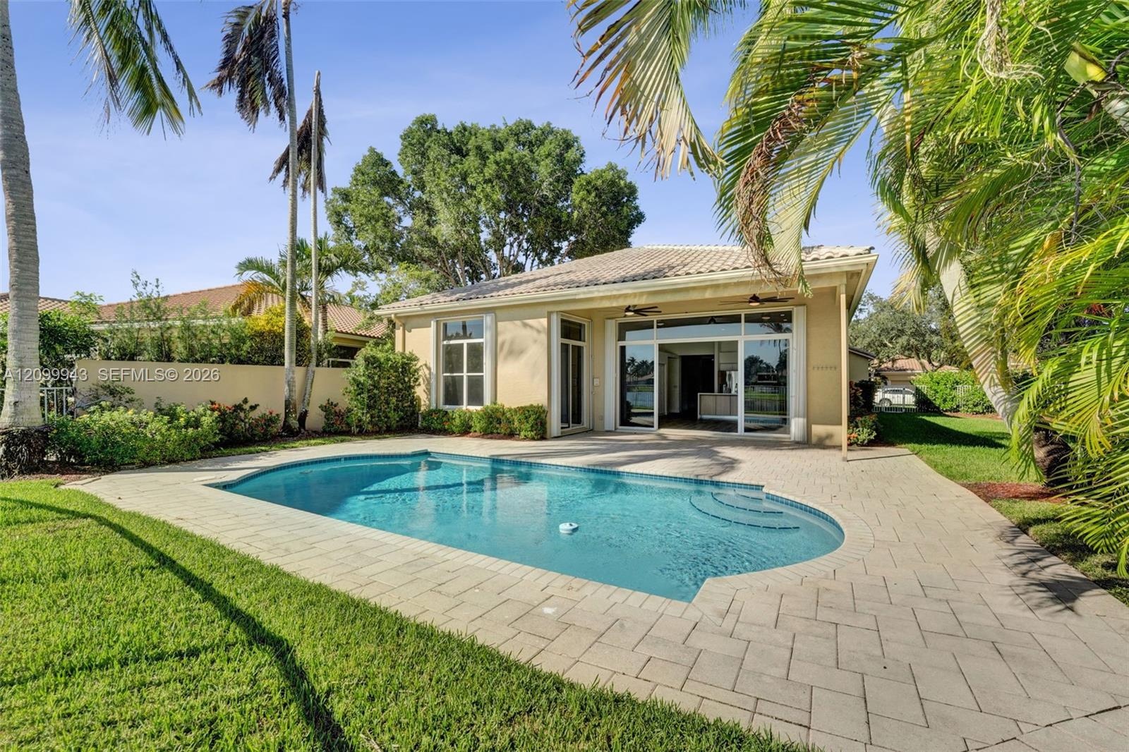In-ground swimming pool with built-in stairs, concrete paver patio, stucco exterior, and multi-panel sliding glass doors