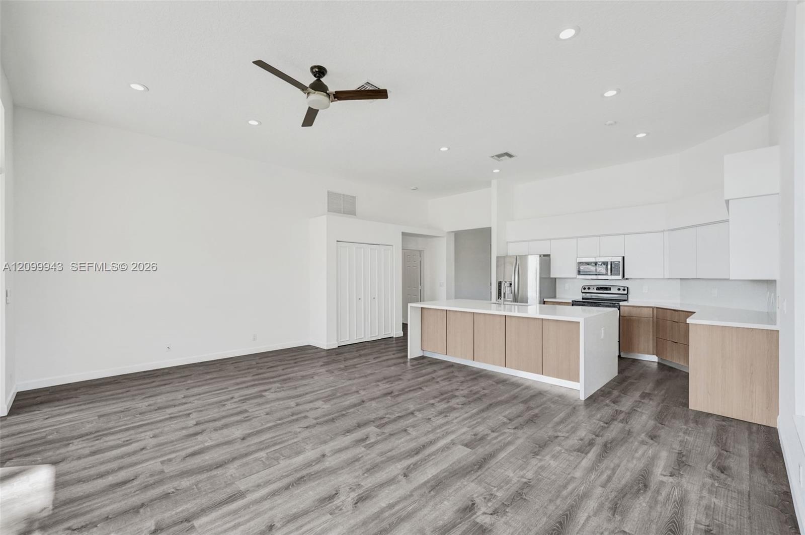 Open-concept interior featuring wood-finish flooring, recessed lighting, and a kitchen equipped with quartz countertops, two-tone cabinetry, and stain