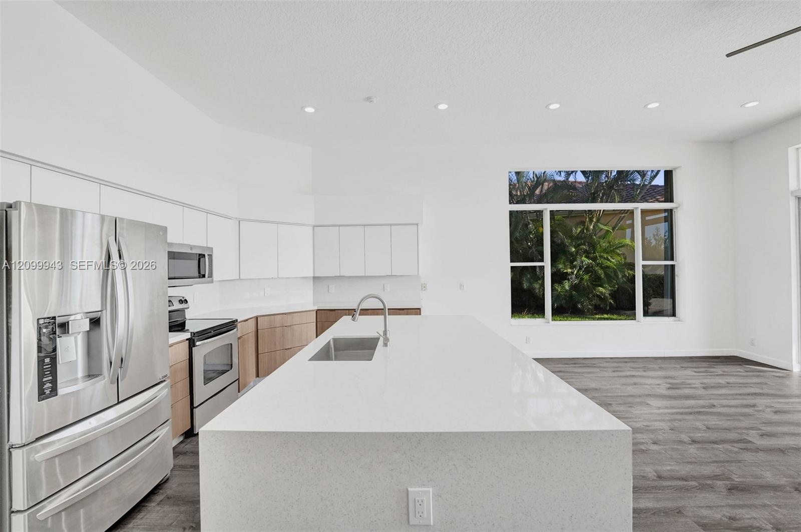 Kitchen featuring a quartz-topped center island with an undermount sink, stainless steel appliances, flat-panel cabinetry, and wood-finish flooring