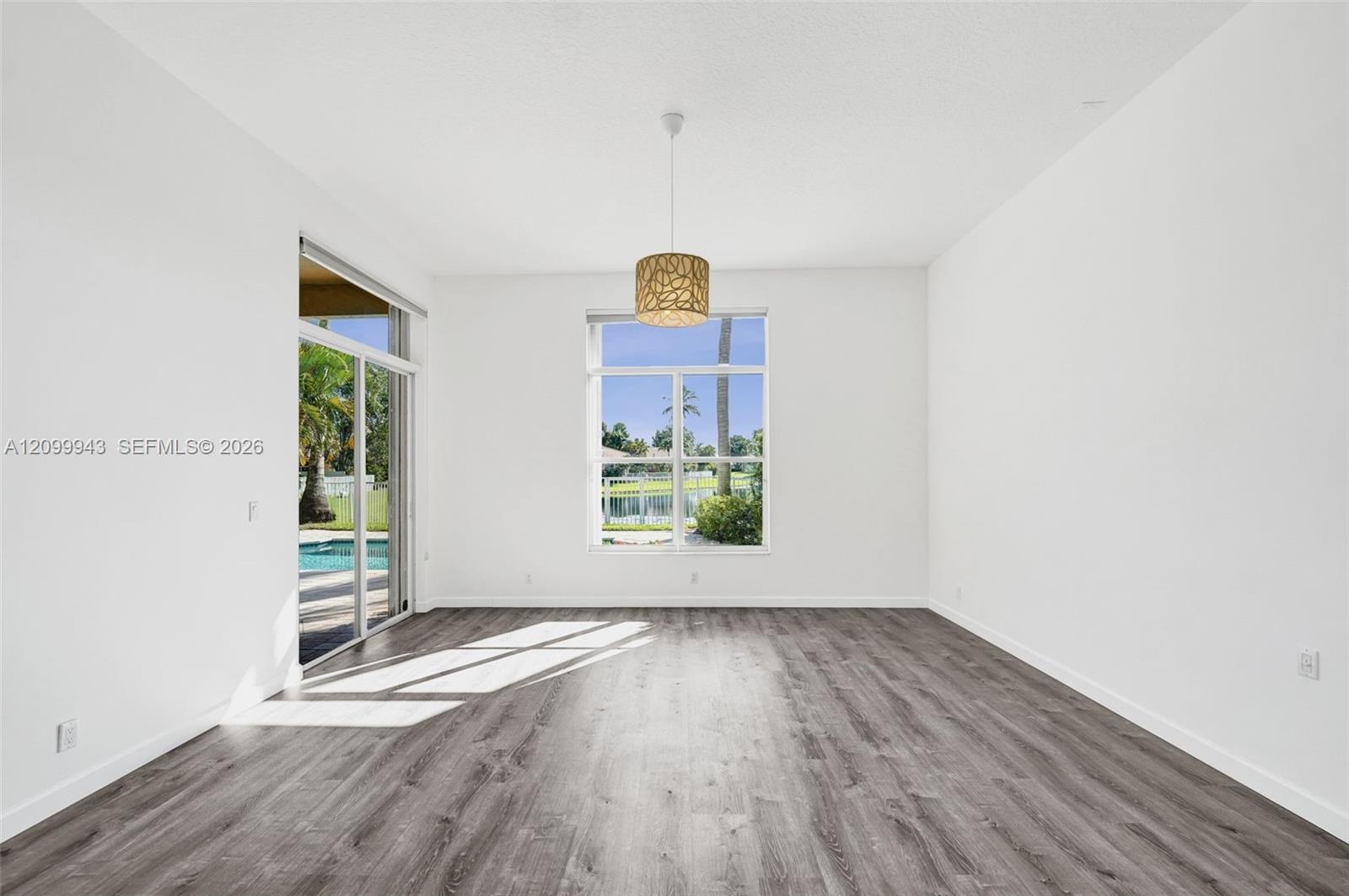 Living area featuring wood-finish flooring, large picture window, sliding glass door, and a textured drum pendant light fixture