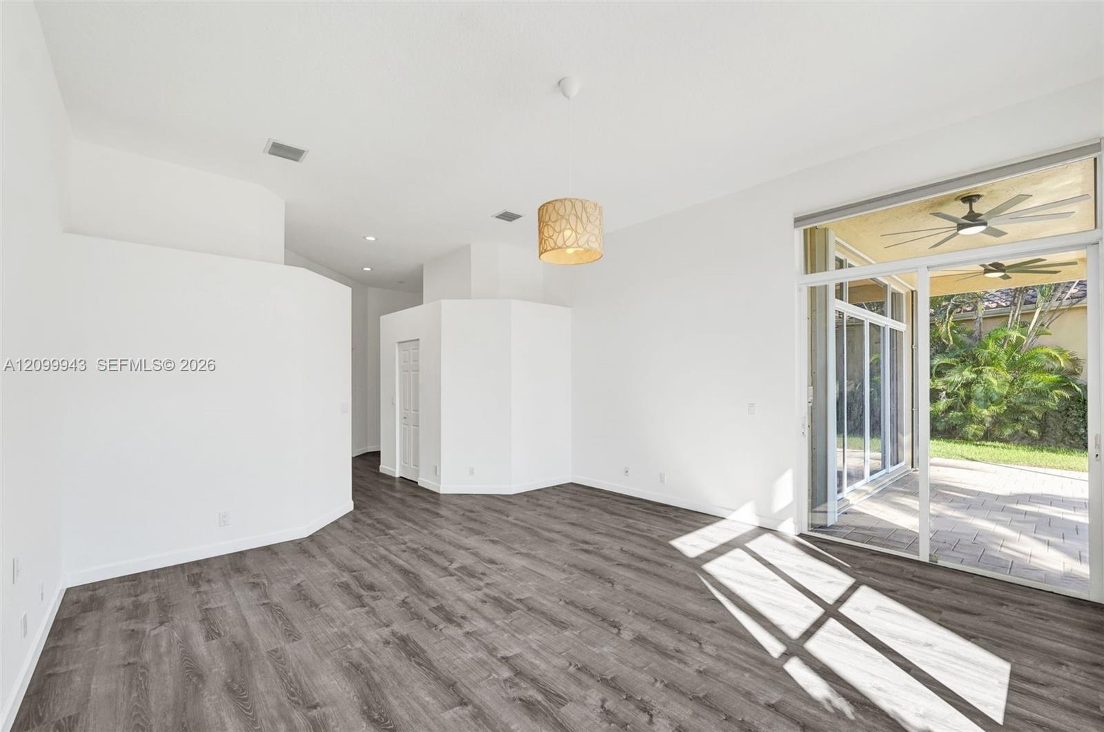 Open interior featuring wood-finish flooring, recessed lighting, a cylindrical pendant fixture, and glass sliding doors