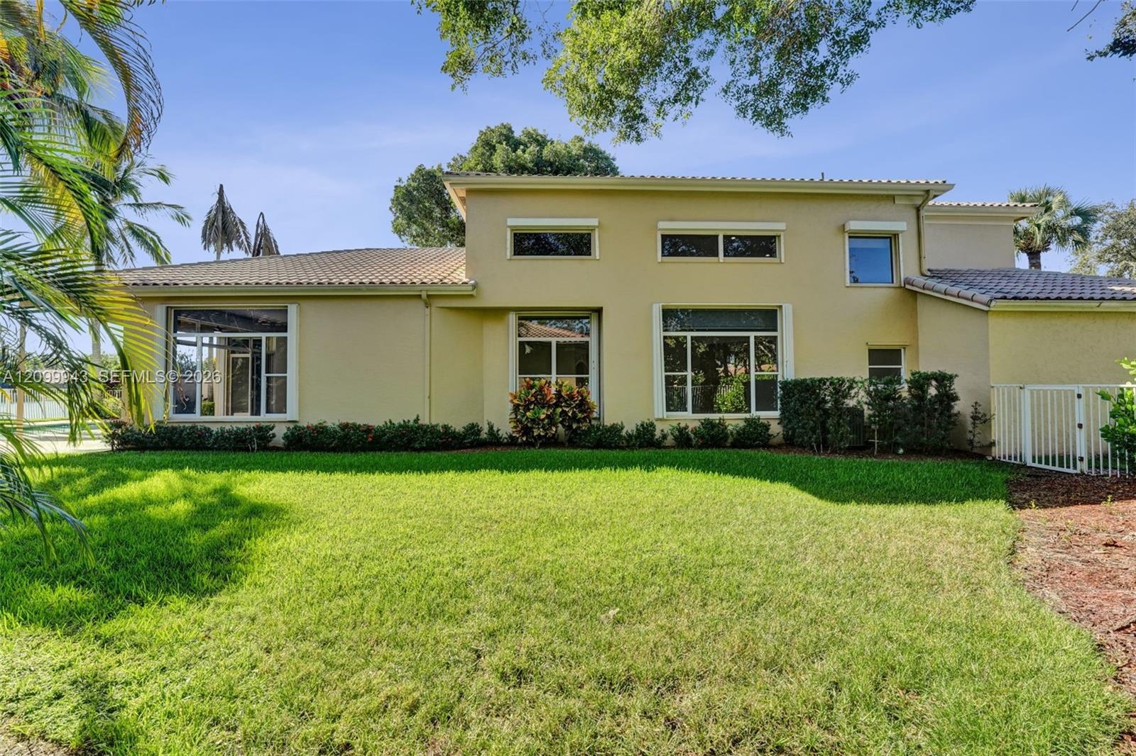 Two-story stucco exterior featuring a tile roof, expansive manicured lawn, multi-pane windows, and privacy fencing