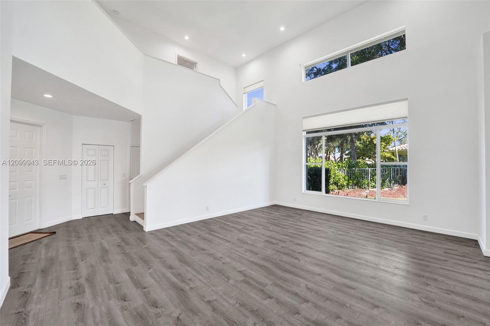 High-ceiling interior featuring wood-finish flooring, recessed lighting, double-height windows, and a staircase with a solid wall banister