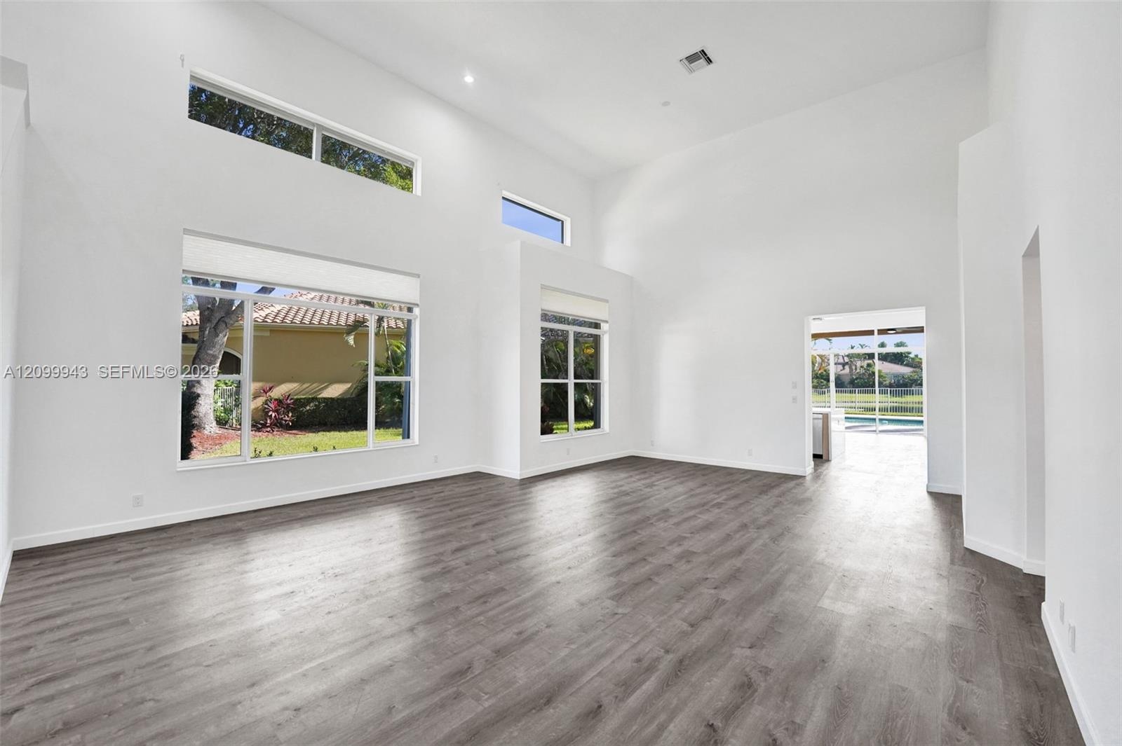 High-ceiling living area featuring wood-finish flooring, multi-level windows, and recessed lighting