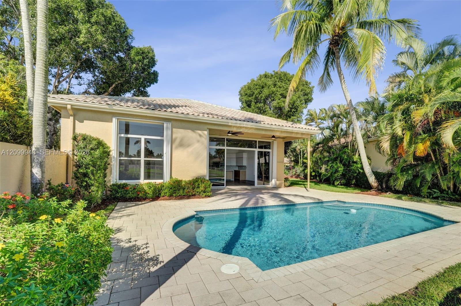 In-ground swimming pool with paver decking, covered patio, tile roof, and mature landscaping