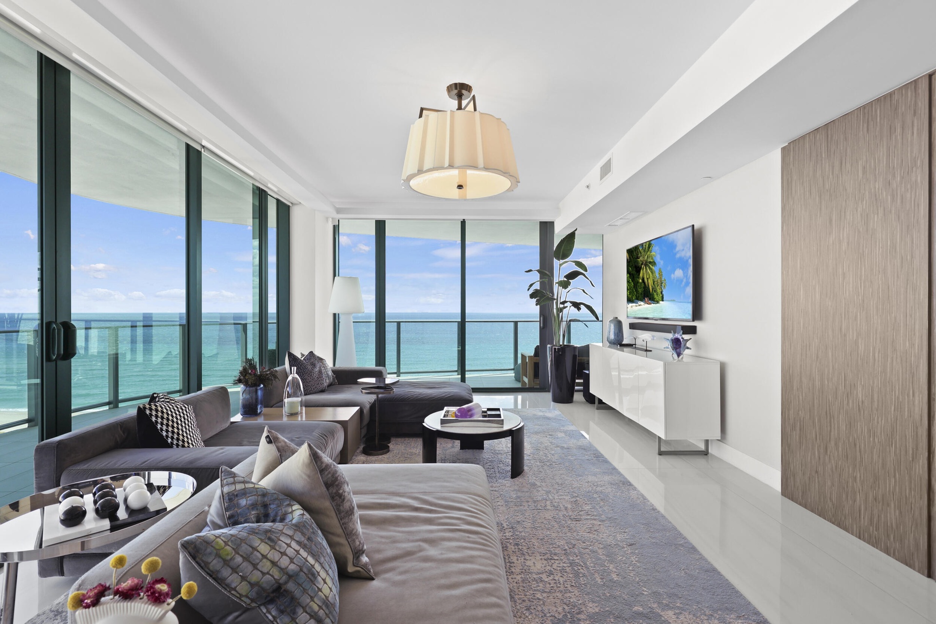 Framed by floor-to-ceiling impact glass, the living room opens seamlessly onto the wraparound balcony, creating an inviting retreat to unwind while en