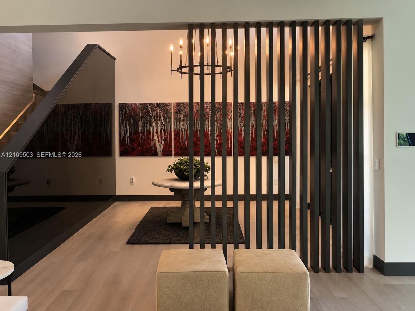 Vertical slatted room divider, wood-finish flooring, high-gloss paneled accent wall, and multi-arm chandelier