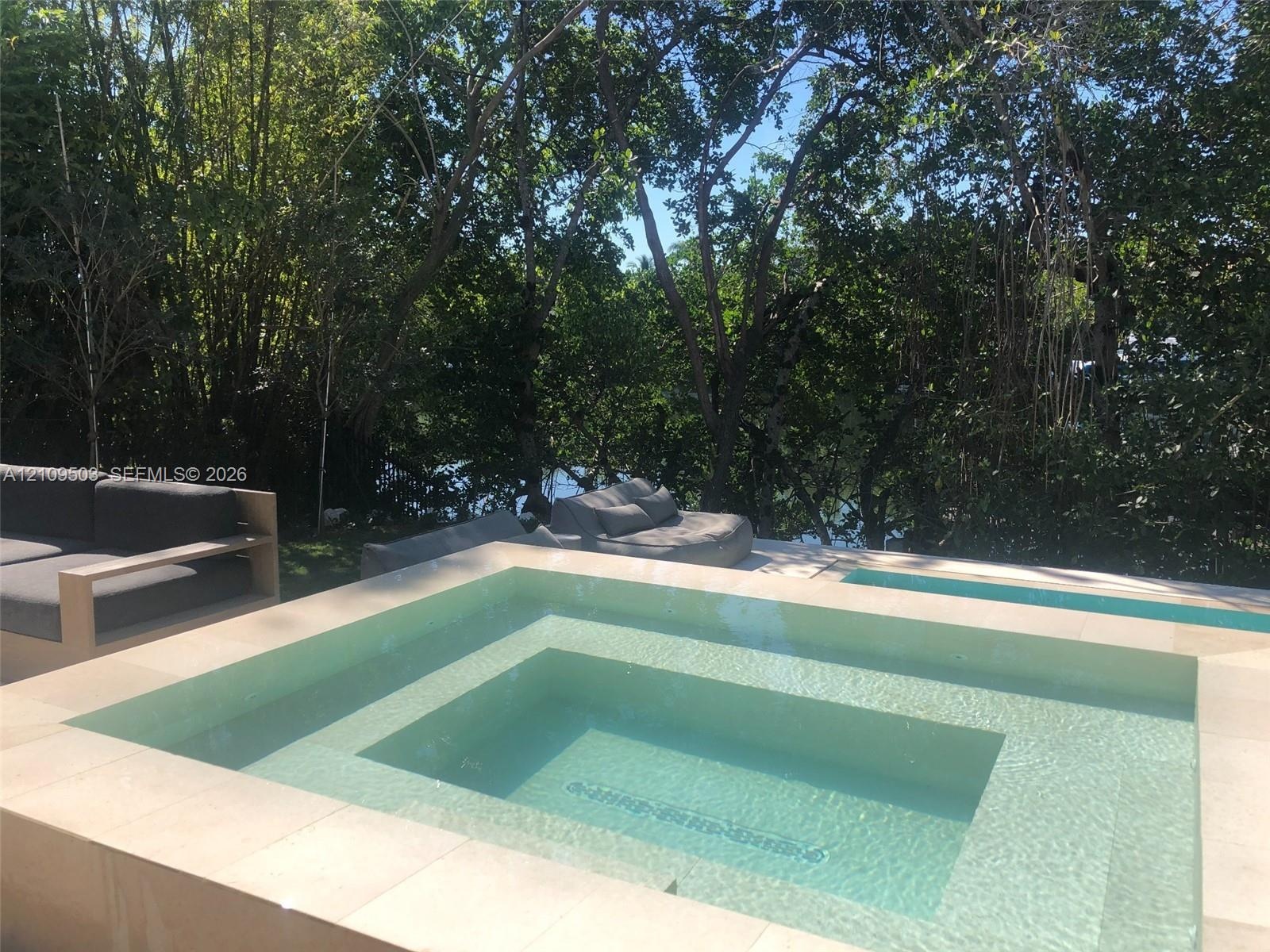 In-ground pool and integrated spa featuring stone coping and surrounding mature trees
