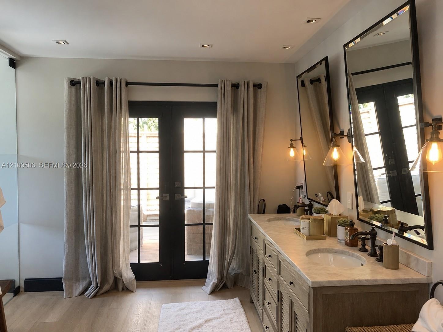 Dual-sink vanity with a stone countertop, recessed lighting, wood-finish flooring, and black-framed glass-paneled double doors