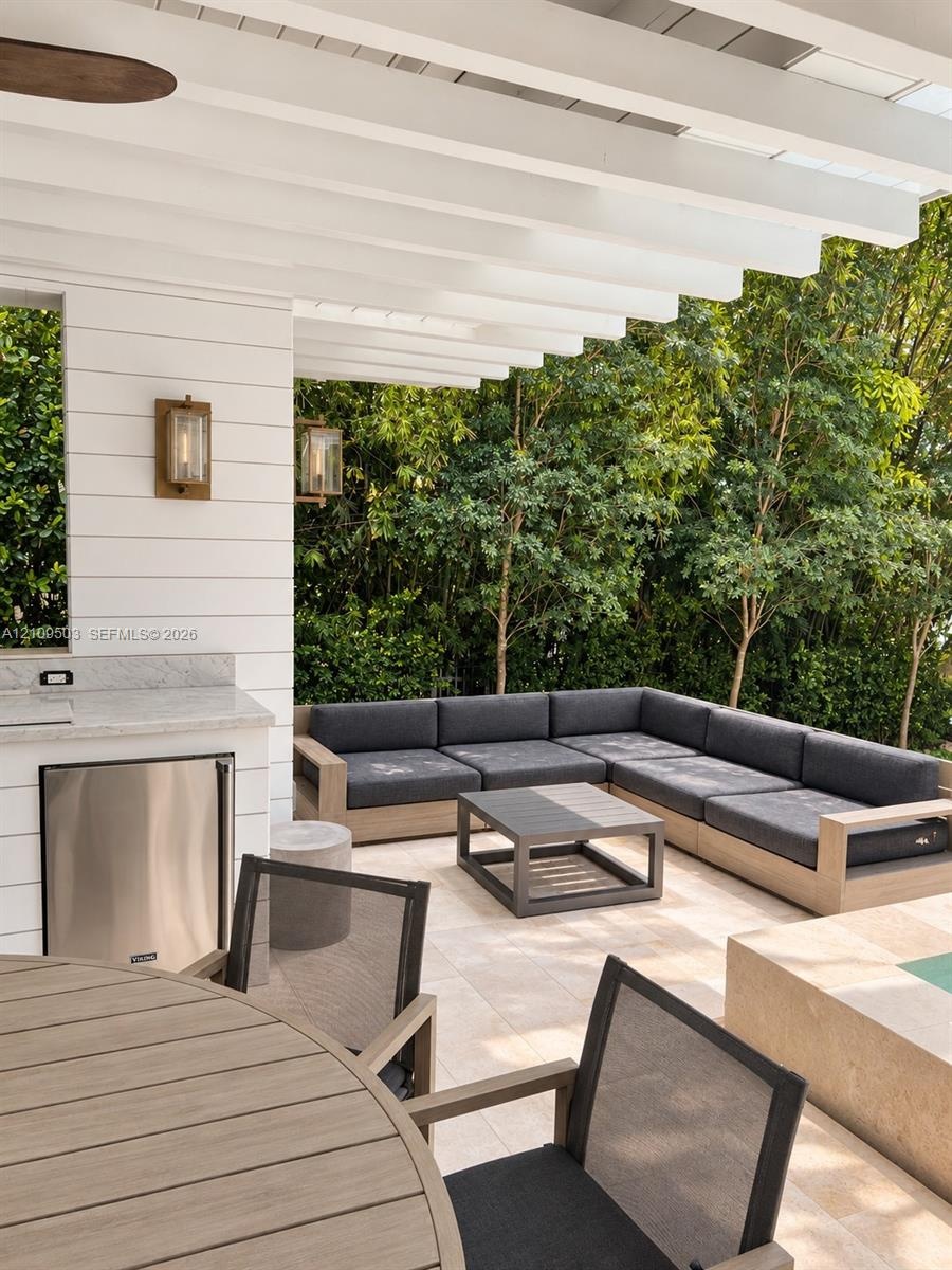Covered patio featuring a white horizontal plank facade, built-in outdoor kitchen with stainless steel refrigeration, natural stone flooring, and wall