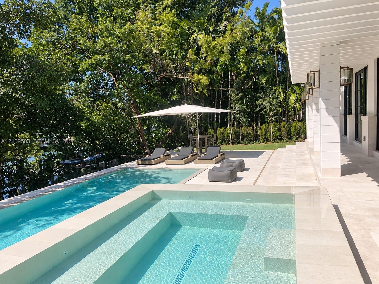 Custom-built swimming pool with integrated spa and stone-paved deck, sheltered by a covered patio with square columns and wall-mounted exterior light 