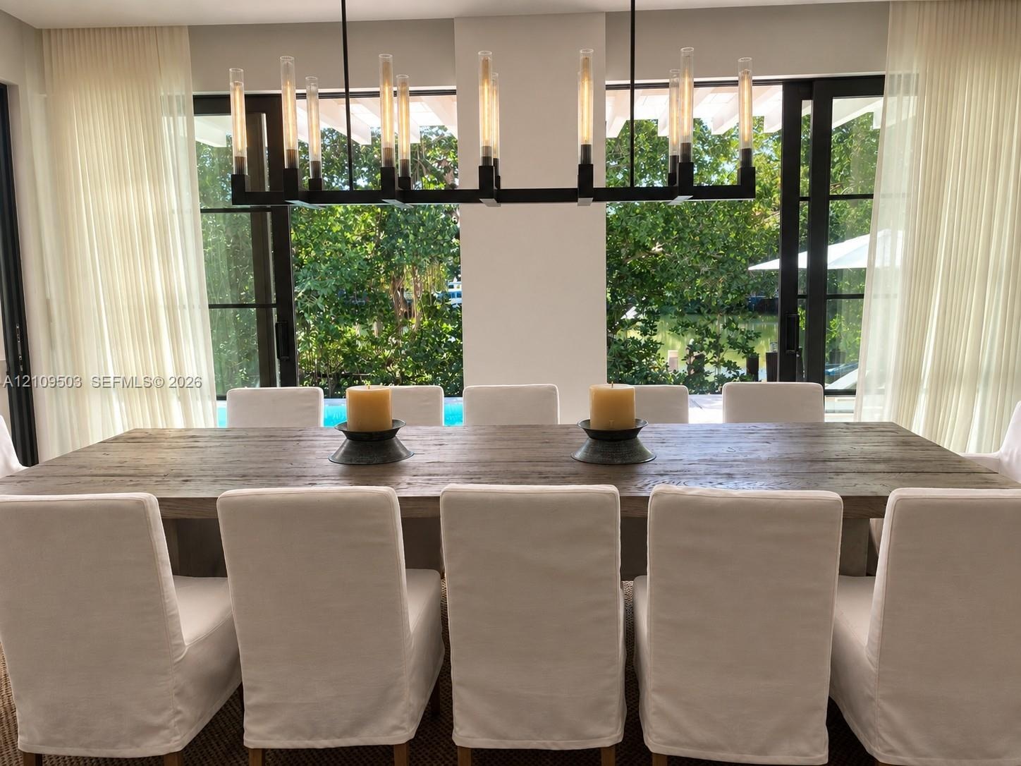 Linear wrought iron chandelier with exposed filament bulbs, floor-to-ceiling metal-framed glass doors, and direct outdoor access