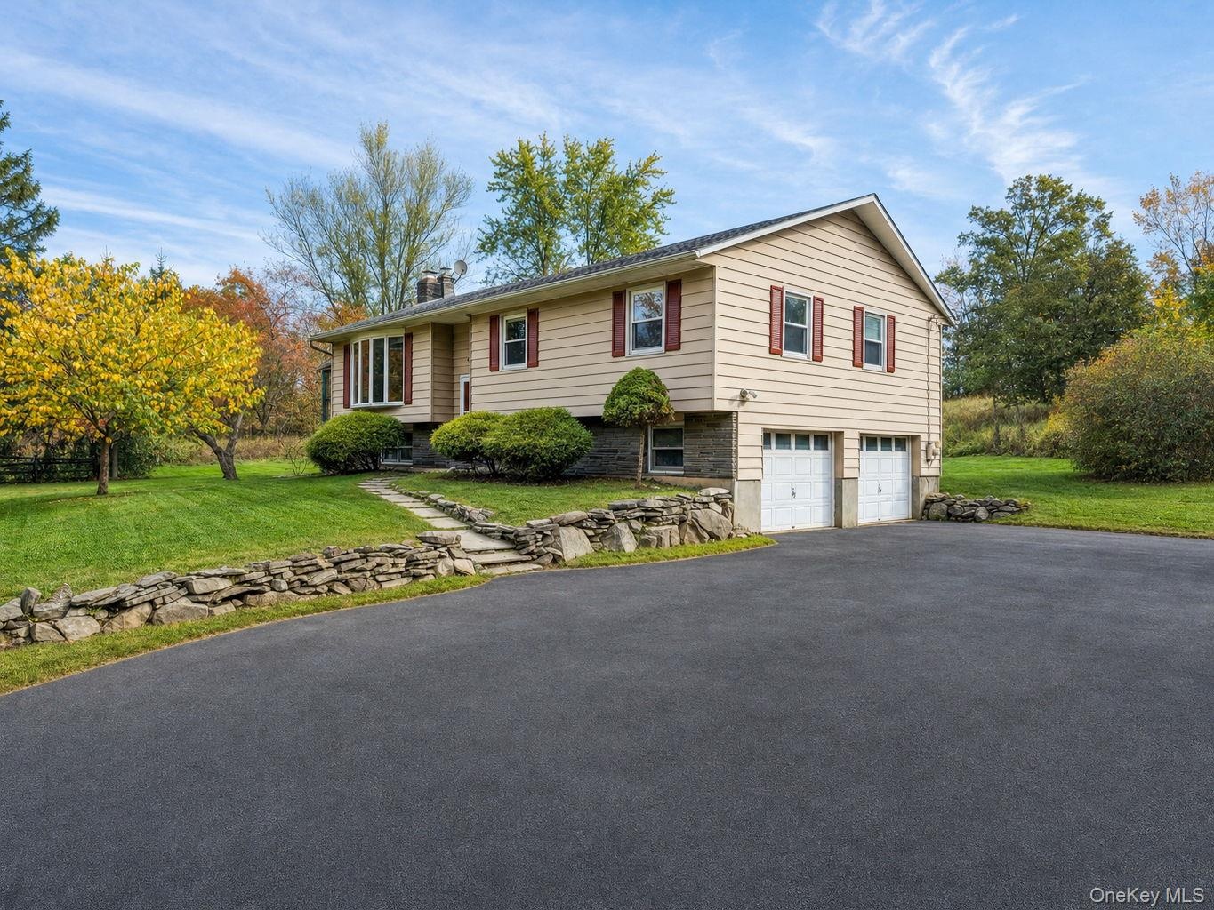 Split-level exterior featuring horizontal aluminum siding, stone veneer accents, an attached two-car garage, paved driveway and a stone retaining wall