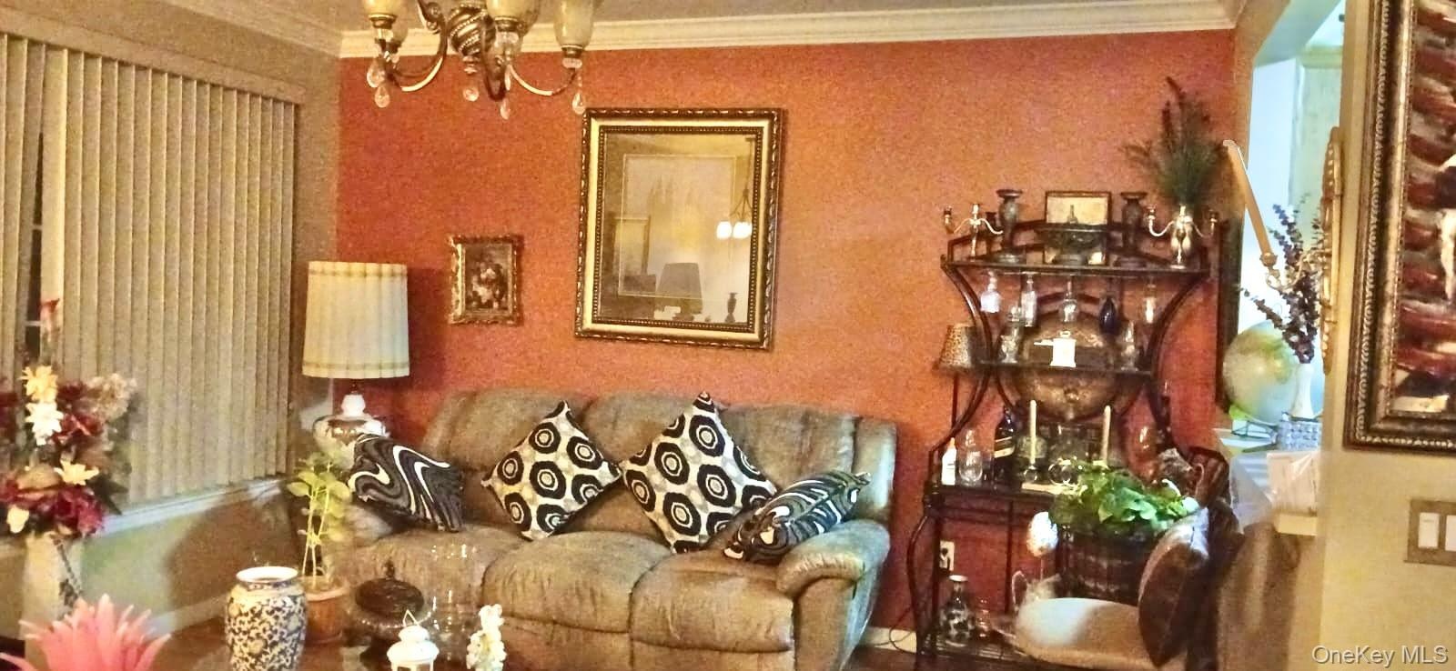 Living area featuring crown molding, textured accent wall, and multi-arm chandelier