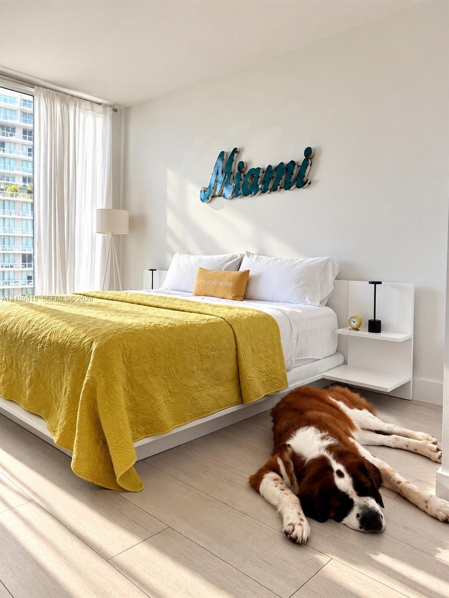 Floor-to-ceiling windows, wood-finish flooring, and built-in bedside shelving units