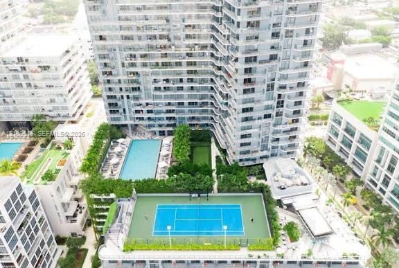 High-rise residential building featuring a blue-surfaced tennis court, swimming pool, landscaped lawn, and multiple levels of private balconies