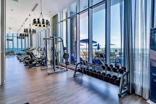 Fitness facility featuring floor-to-ceiling windows, wood-finish flooring, and industrial-style multi-arm chandeliers