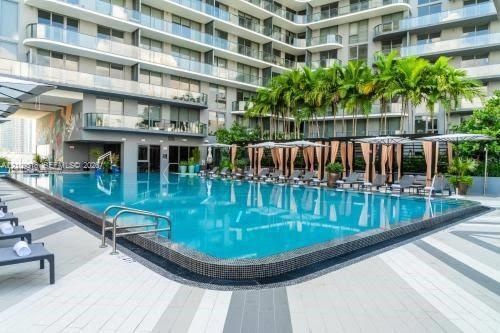 Swimming pool with tile surround, multi-story structure with glass-panel balconies, concrete patio decking, and established palm trees