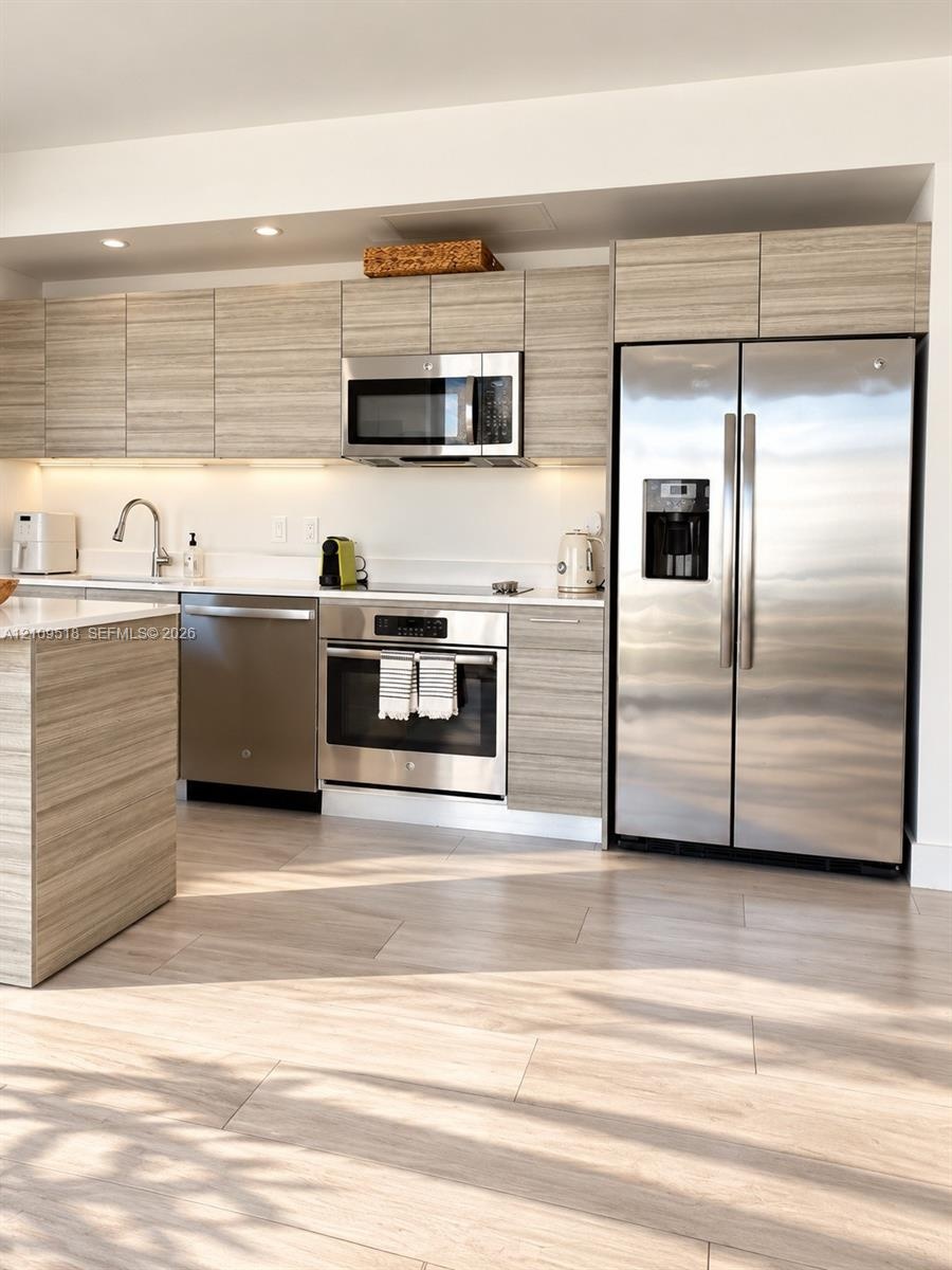 Kitchen featuring horizontal-grain wood-finish cabinetry, stainless steel appliances, solid-surface countertops, recessed ceiling lighting, and wood-f