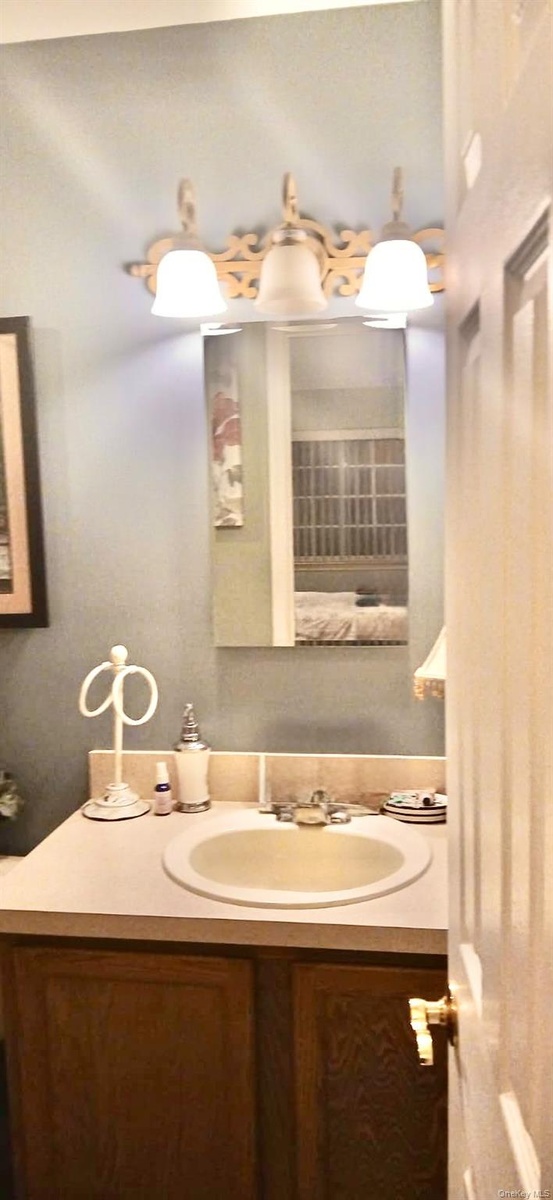 Vanity featuring wood-finish cabinetry, a white integrated countertop and sink, a three-light decorative wall fixture, and a rectangular mirror