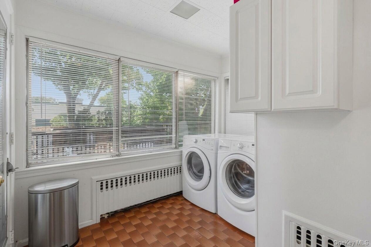 Laundry area featuring full-size washer and dryer, tile flooring, window treatments, and white overhead cabinetry