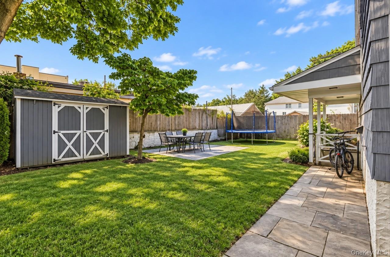 Expansive backyard featuring a manicured lawn, established trees, and a gray storage shed with white crossbuck doors