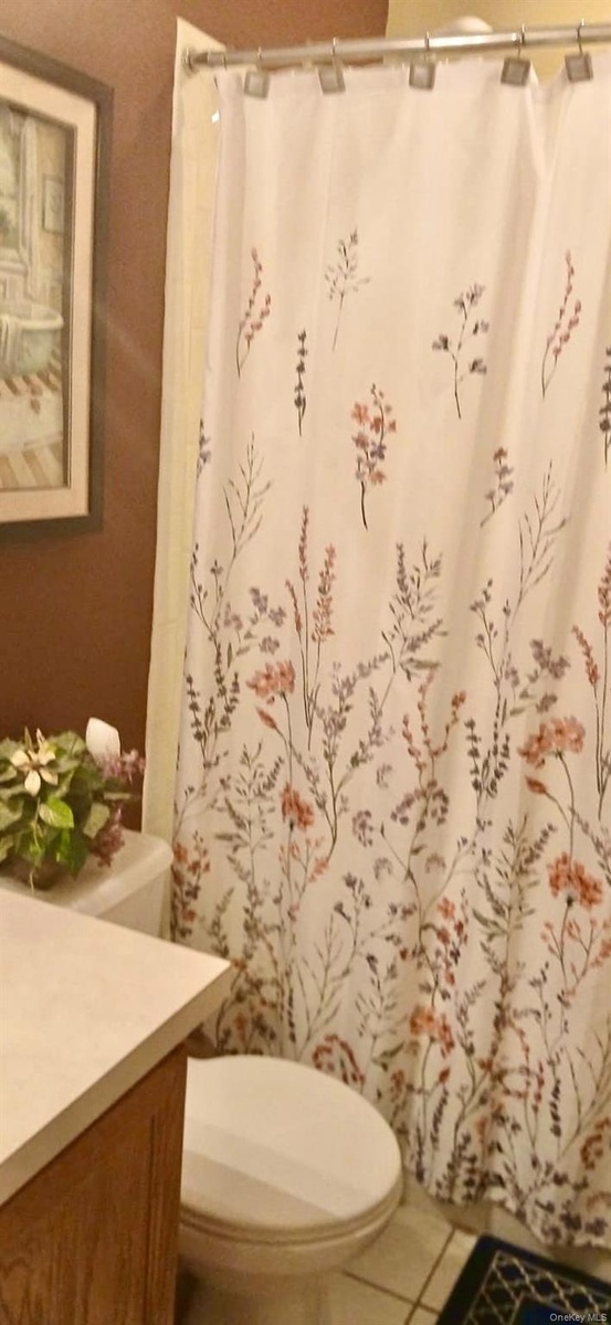 Bathroom featuring a vanity with a countertop, toilet, and a tub enclosure with a shower rod