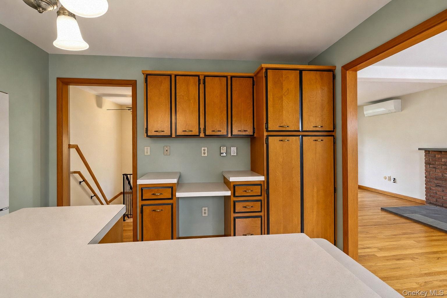 Kitchen workspace featuring natural wood-finish cabinetry, a built-in floor-to-ceiling pantry, solid surface countertops, and an integrated desk area 