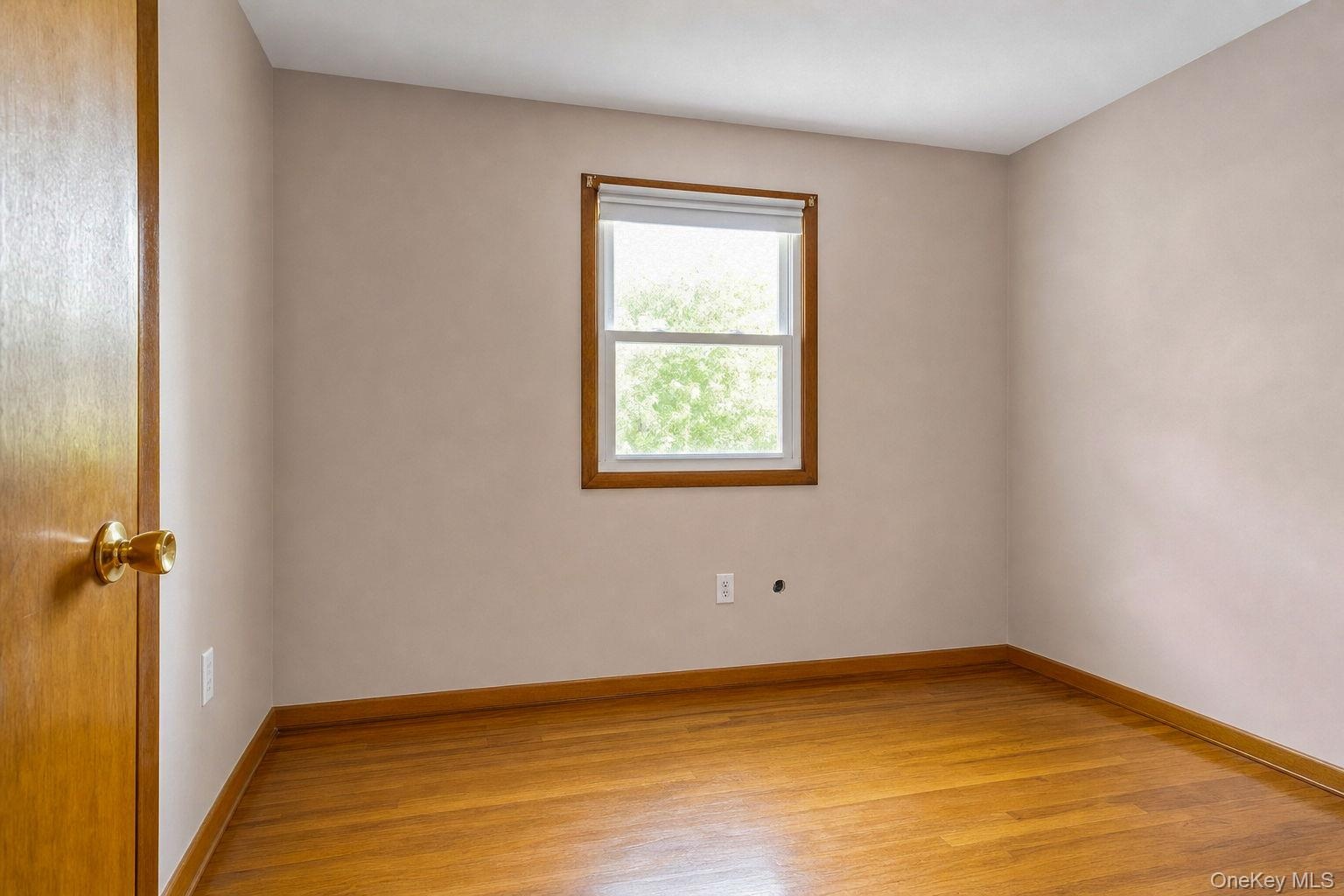 Room featuring hard wood flooring, neutral wall paint, and a single-hung window with wood trim