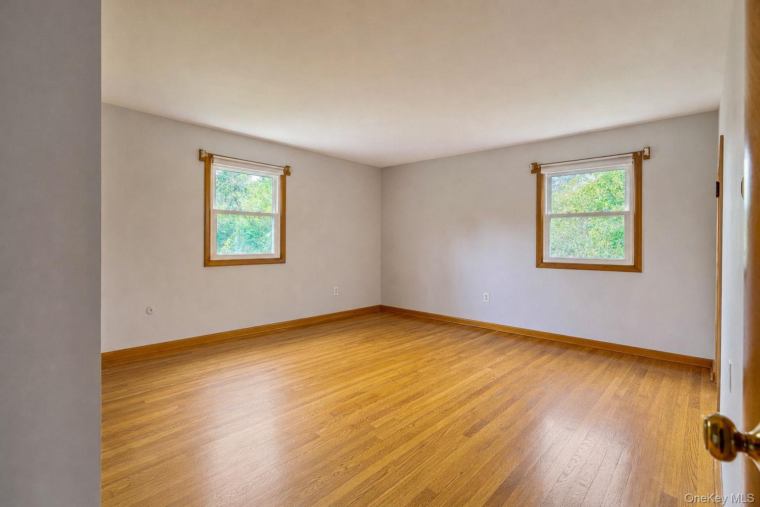 Neutral-toned interior space featuring hard wood flooring, two windows with wood-trim framing, and a smooth ceiling