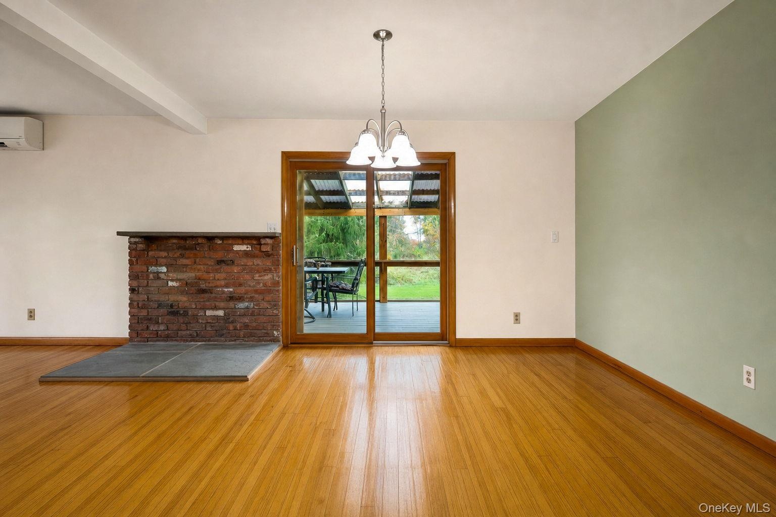 Hard wood flooring, exposed red brick fireplace hearth, sliding glass door to screened porch, multi-light chandelier, and accent wall