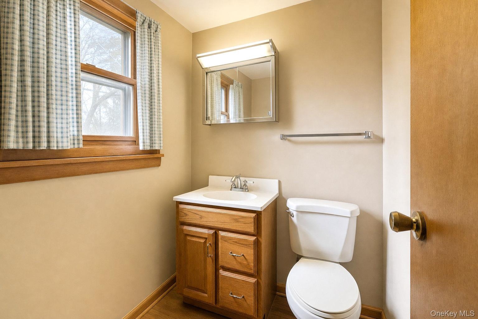 Wood-finish vanity with a white countertop and integrated sink, mirrored medicine cabinet, dual-handle faucet, and wooden window trim