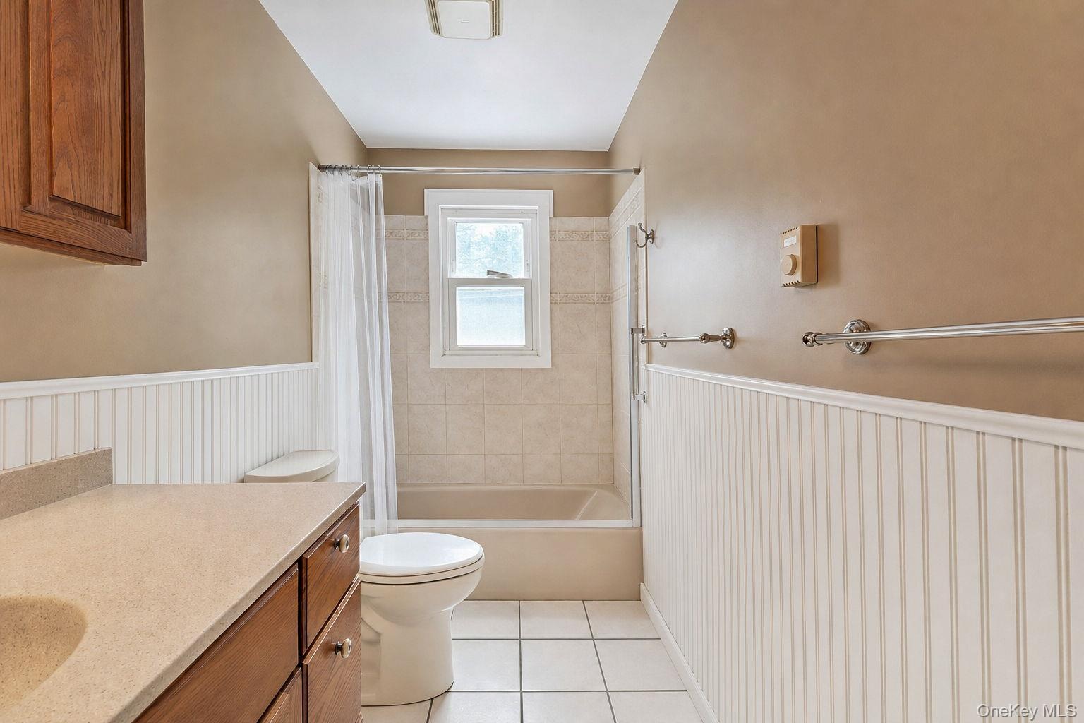 Bathroom featuring beadboard wainscoting, wood-finish cabinetry, a solid surface countertop with an integrated basin, tile flooring, and a tub-shower 
