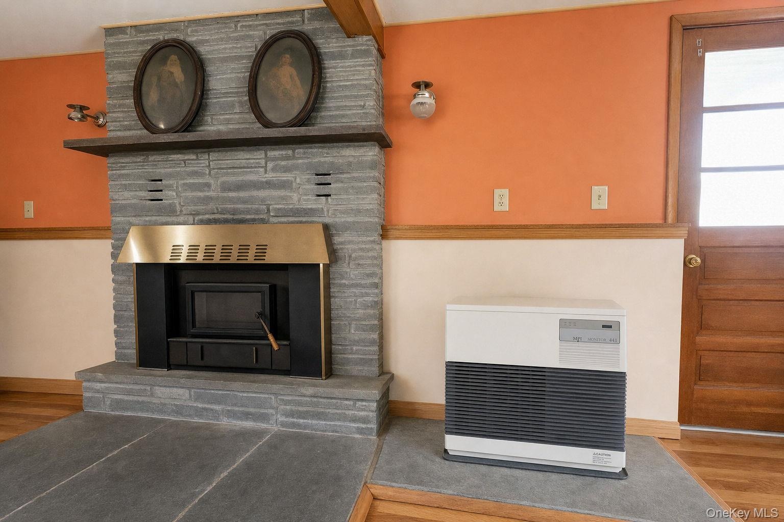 Stone-clad fireplace with a built-in metal firebox, natural stone hearth, kerosine heater, wood-finish flooring, wood-framed multi-pane door, and dual