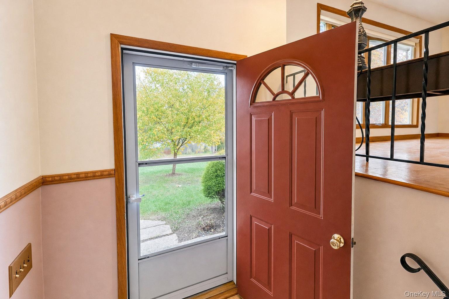 Entryway featuring a solid wood door with a semi-circular glass insert, a storm door, wood-trimmed door casing, decorative chair rail, and a wrought i