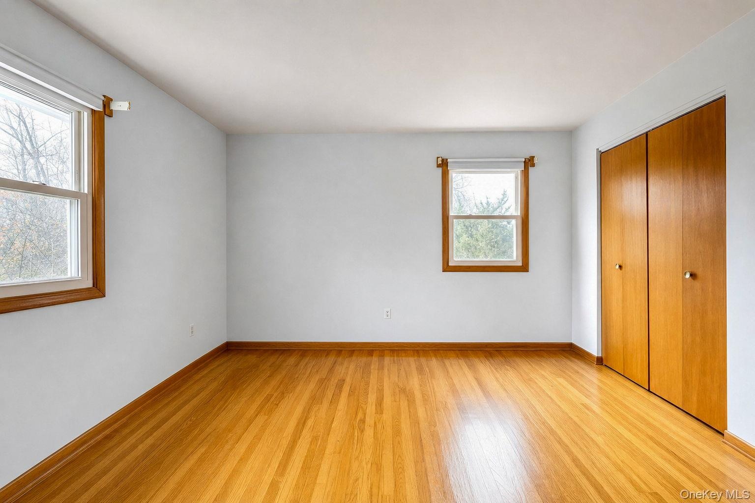 Hard wood flooring, double-door wood closet, and windows with wood-tone casing and additional closet