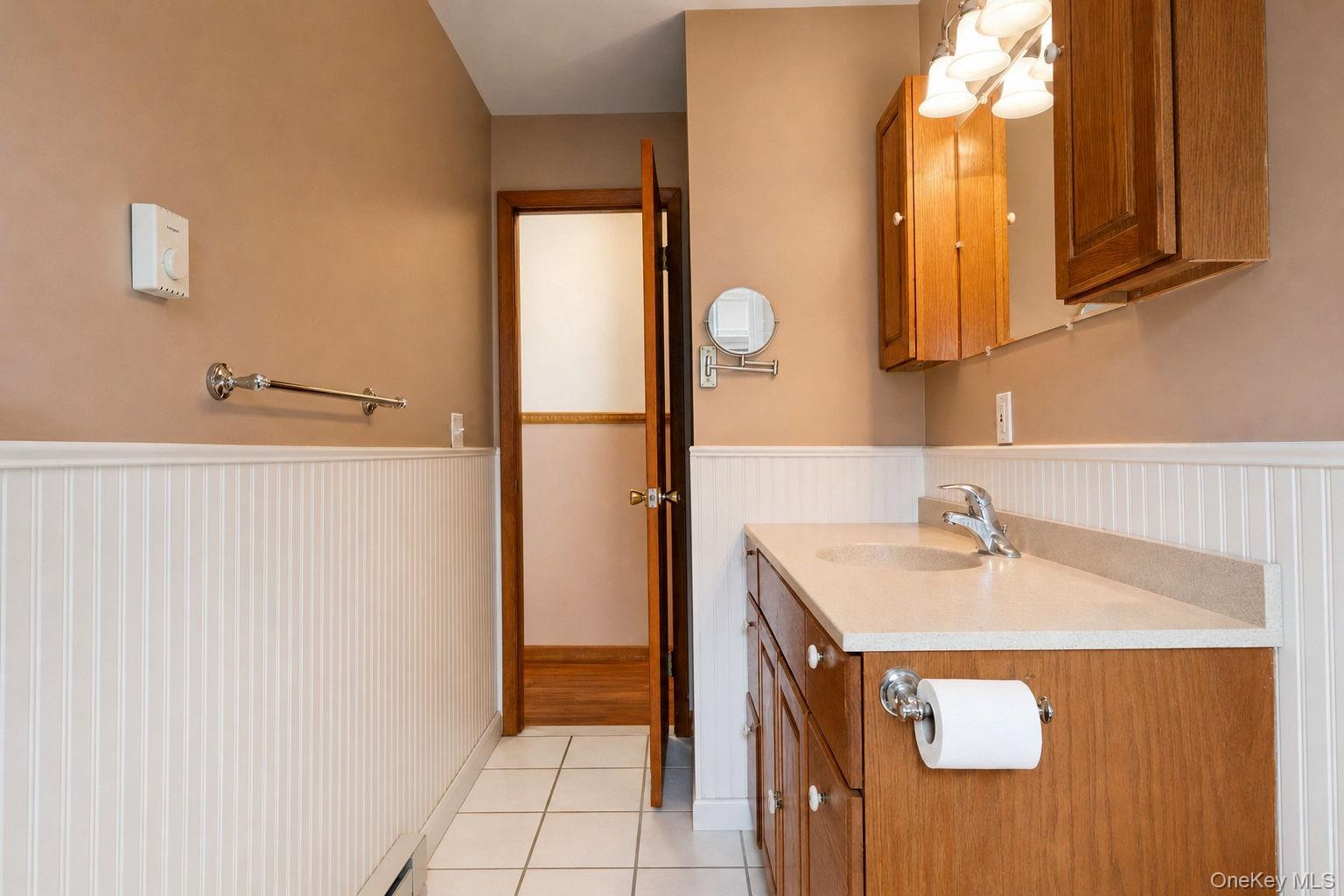 Main bathroom featuring beadboard wainscoting, a wood-finish vanity with a solid-surface countertop, an integrated sink, and tile flooring